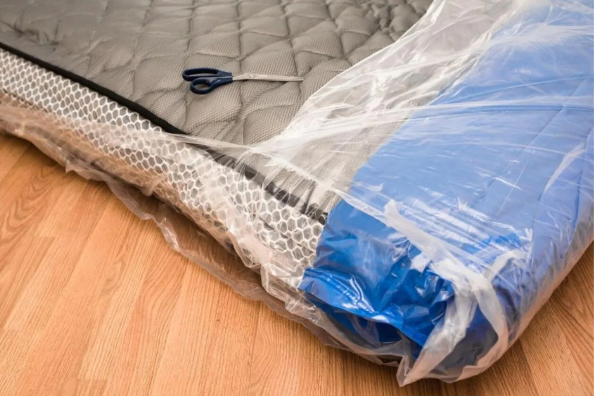 Partially compressed mattress wrapped in plastic with scissors nearby, illustrating the process of preparing a memory foam mattress for compression and packing