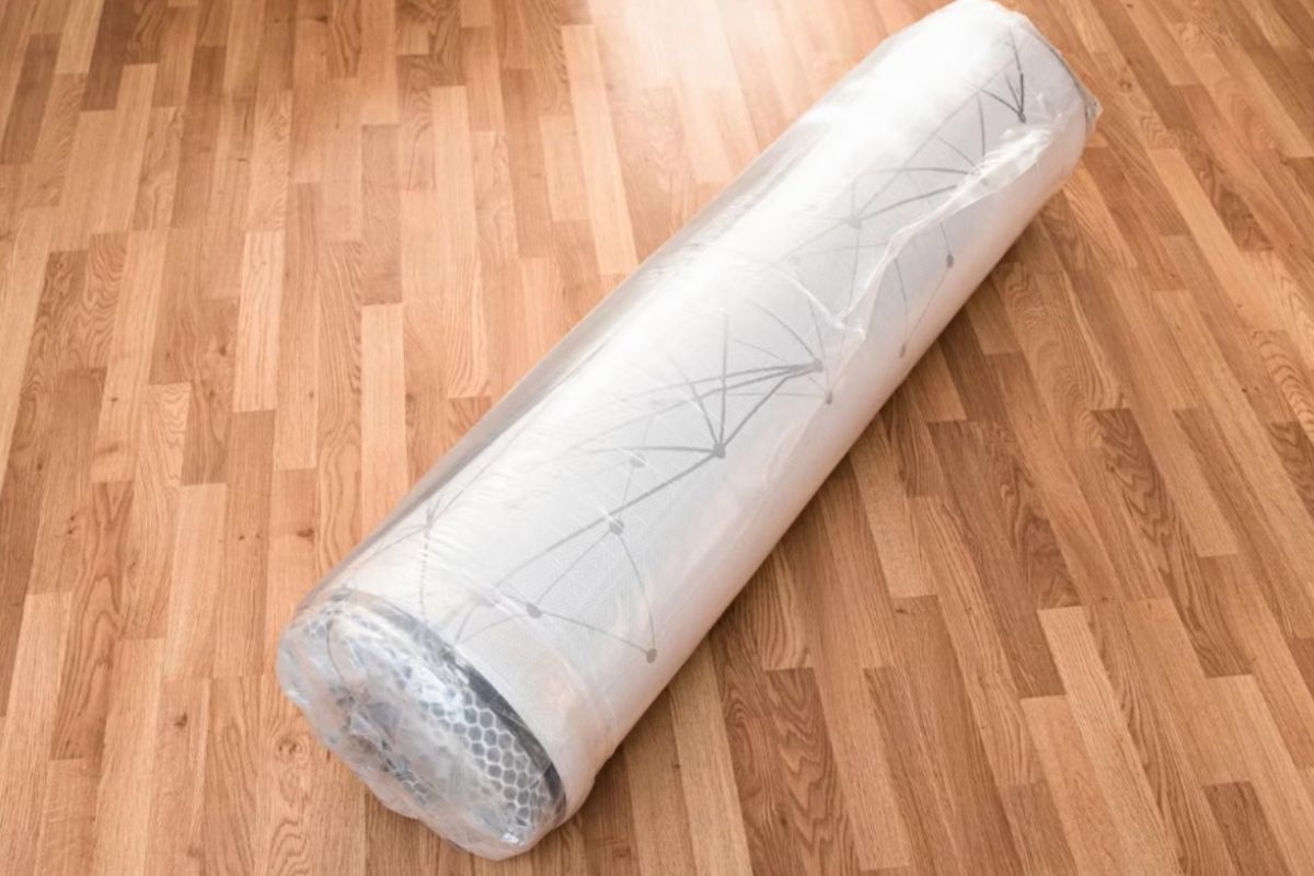 Rolled and vacuum-sealed memory foam mattress on a floor, showing the compact form used when compressing a mattress for storage or moving