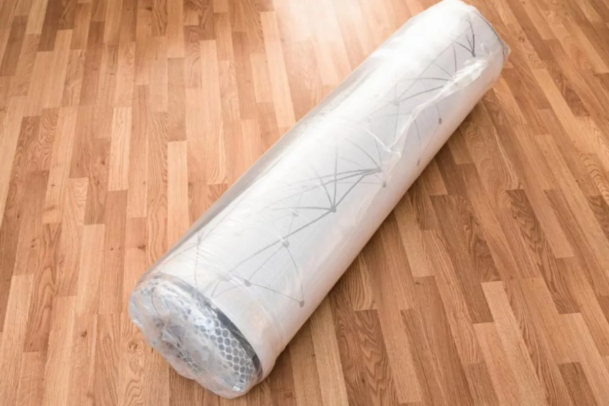Rolled and vacuum-sealed memory foam mattress on a floor, showing the compact form used when compressing a mattress for storage or moving