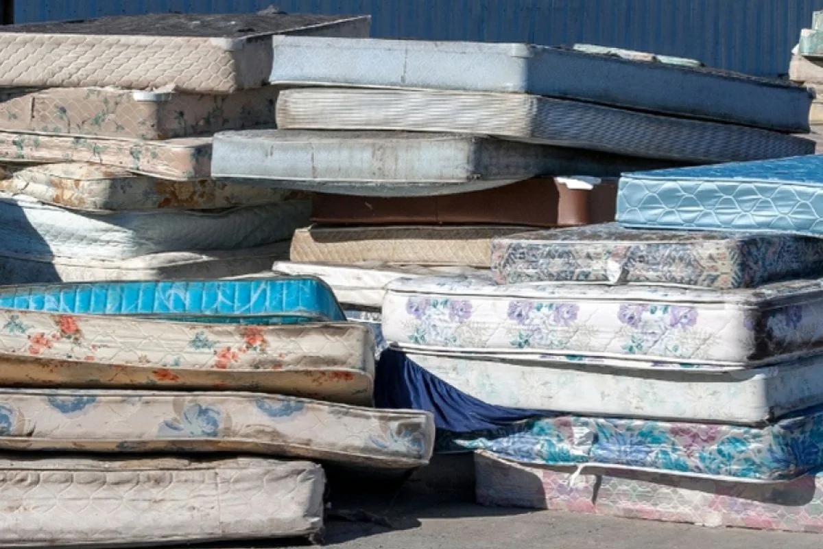 Pile of discarded mattresses at a recycling or waste facility, highlighting responsible disposal and recycling methods for old memory foam mattresses