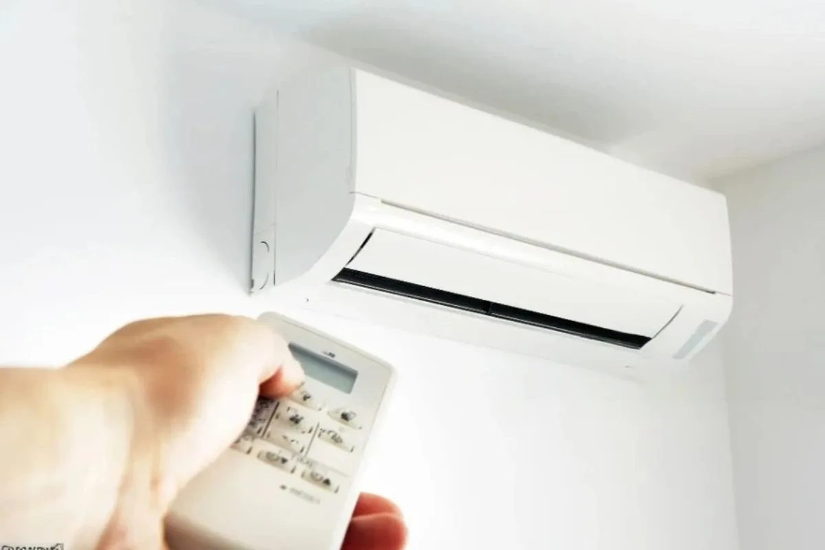 Person adjusting an air conditioner with a remote control, demonstrating how lowering room temperature can improve comfort on a memory foam mattress