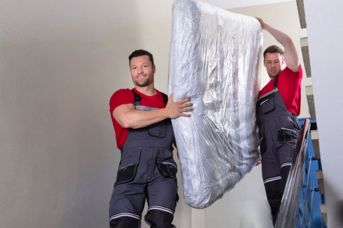 Two movers carrying a wrapped hybrid mattress down a staircase, demonstrating safe mattress handling during a move.