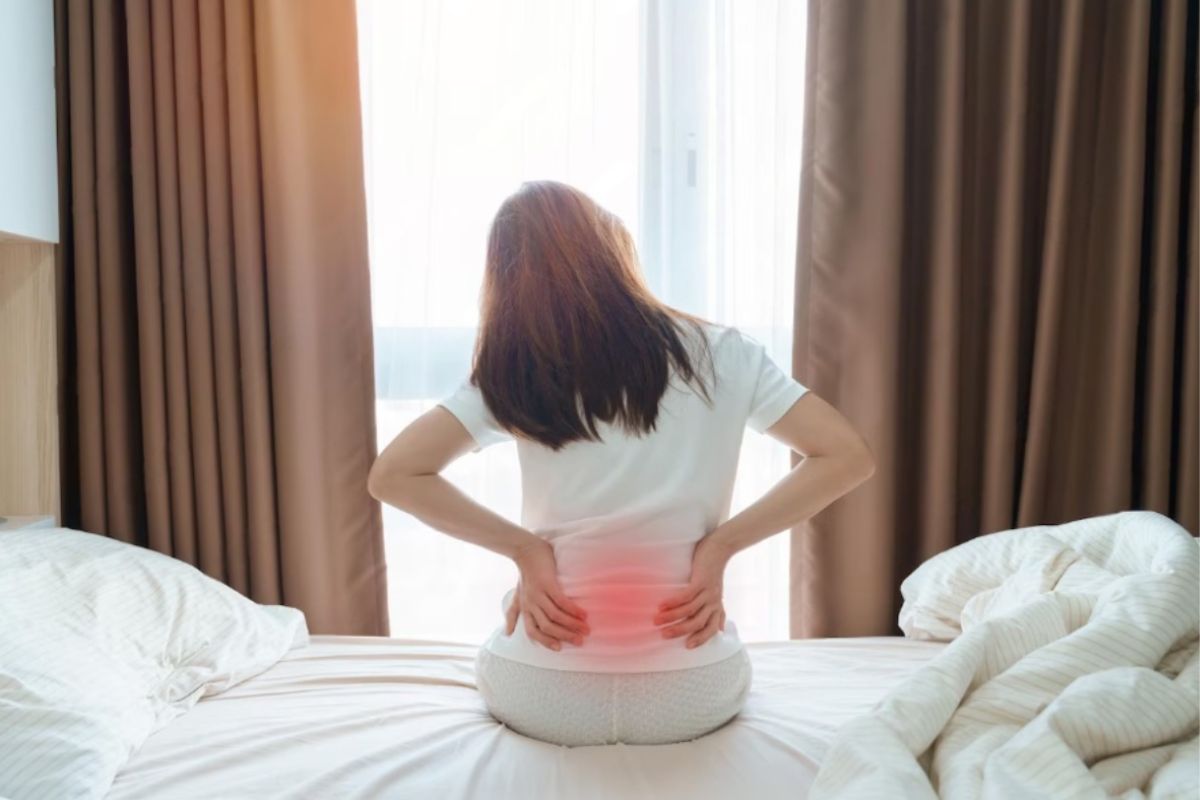 Person experiencing lower back discomfort while sitting on a bed, illustrating potential issues when sleeping on a memory foam mattress before it fully expands