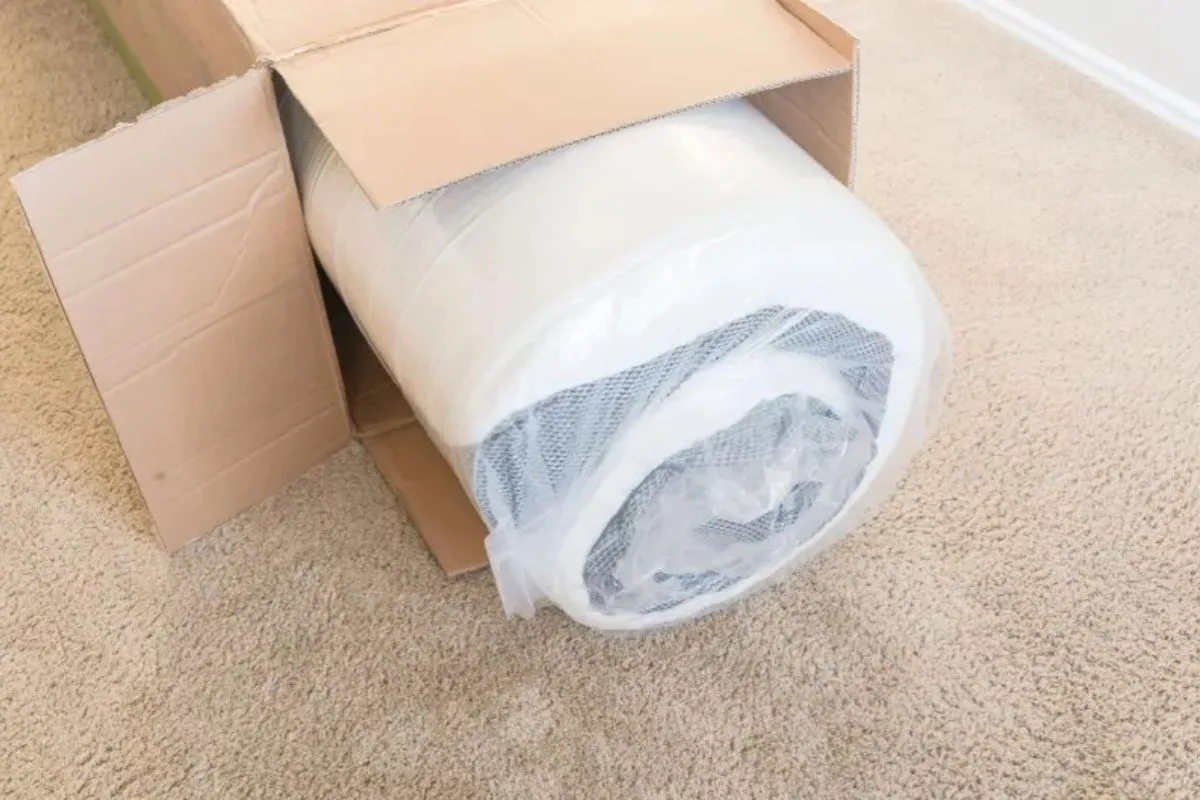 Rolled hybrid mattress being unpacked from a shipping box, demonstrating the bed-in-a-box delivery process common with modern hybrid mattresses