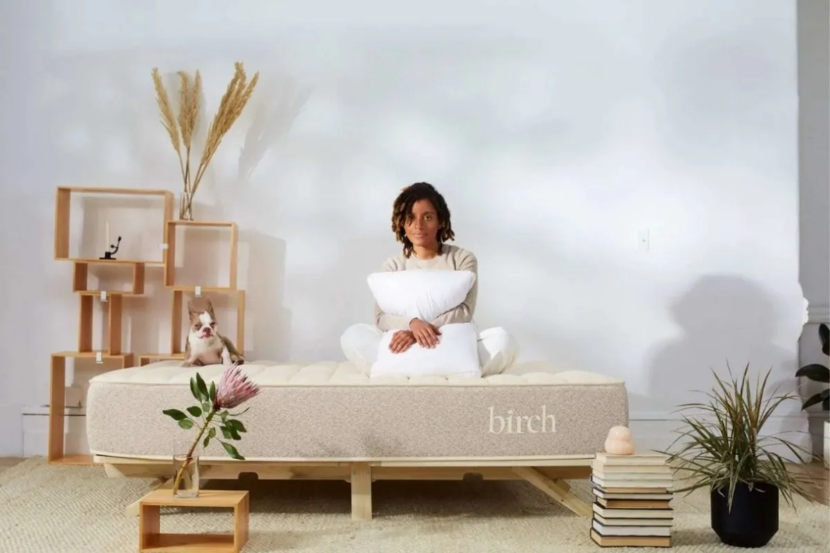 What Time Should I Go to Bed? Find Your Optimal Sleep Schedule Person sitting on a mattress with pillows, symbolizing the role of a comfortable sleep environment in maintaining a healthy bedtime routine