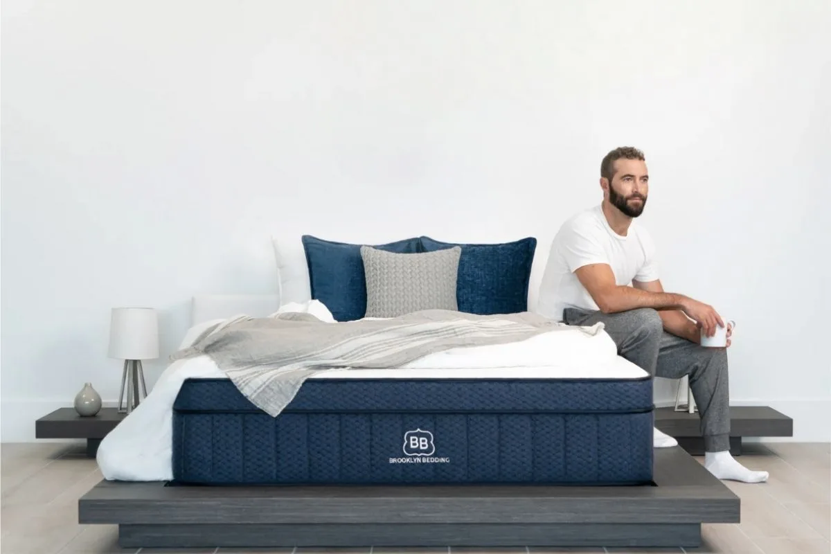 Man sitting on the edge of a Brooklyn Bedding mattress, highlighting how mattress comfort and support can influence sleep quality and duration for adults