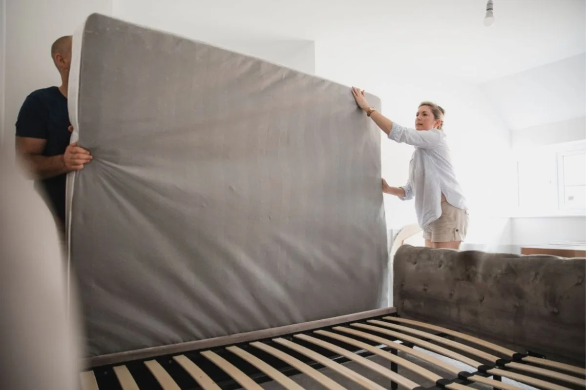 How Often Should You Turn an Innerspring Mattress? Two people rotating a mattress on a bed frame, demonstrating how to safely turn an innerspring mattress during routine maintenance
