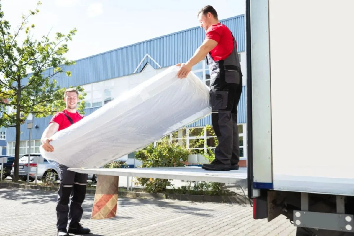Professional movers loading a wrapped memory foam mattress into a moving truck for secure transportation