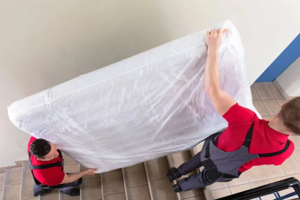 Moving team carrying a plastic-wrapped memory foam mattress down a staircase to prevent tears and make transport easier