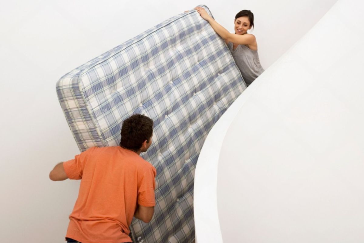 Two people rotating and maneuvering a mattress through a stairwell, demonstrating safe techniques for moving a memory foam mattress between floors