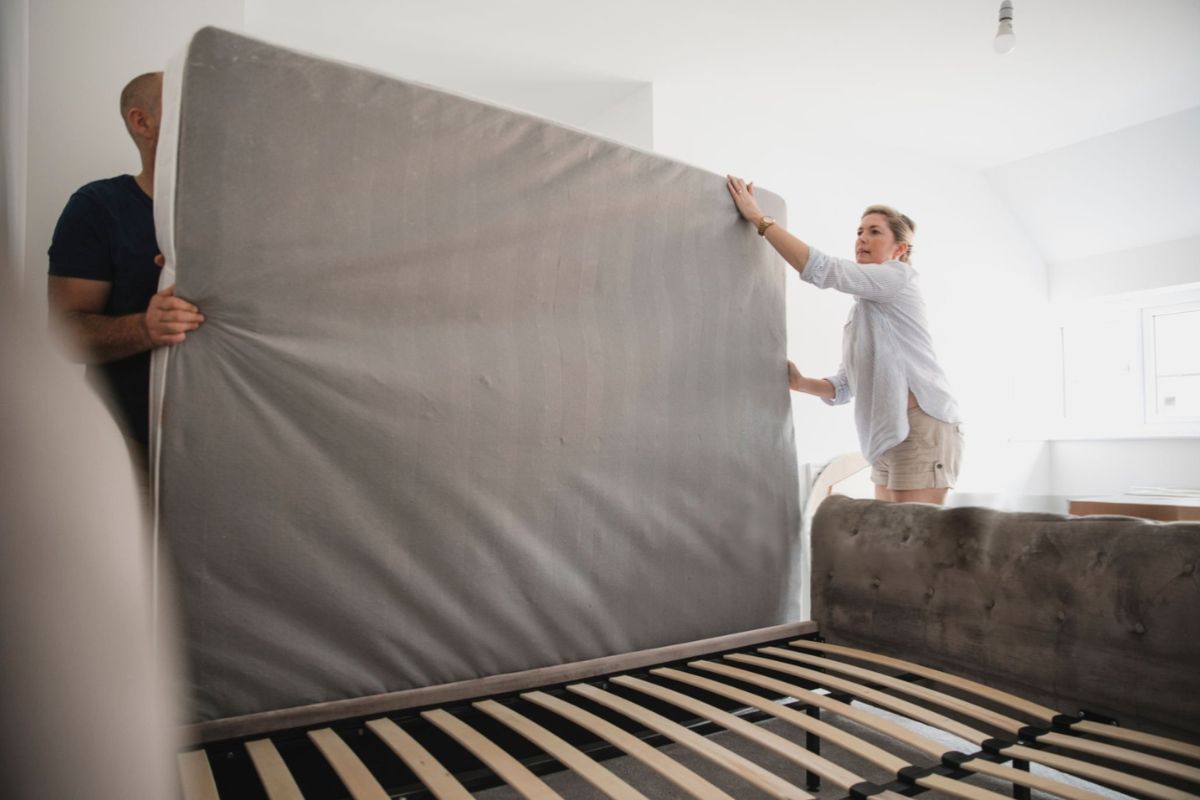 People setting up a mattress on a bed frame, representing practical considerations like mattress weight, handling, and ease of installation when choosing between innerspring and memory foam models