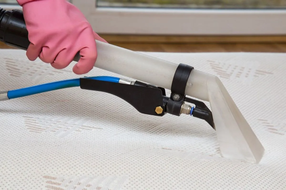 Deep cleaning a latex mattress with an upholstery extraction tool to remove dirt, stains, and allergens