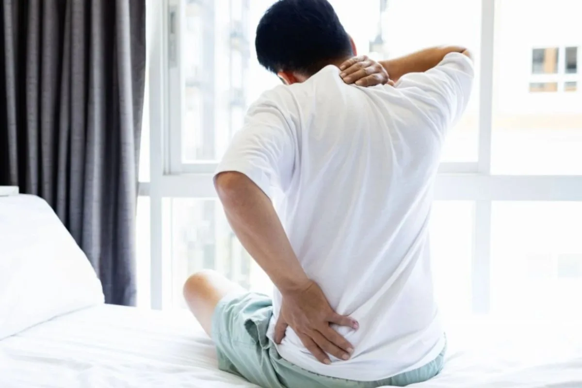Hybrid or Memory Foam Mattress for Back Pain: Which Is Better? Individual experiencing back pain while sitting on a bed, highlighting the impact an unsupportive mattress can have on spinal alignment and discomfort