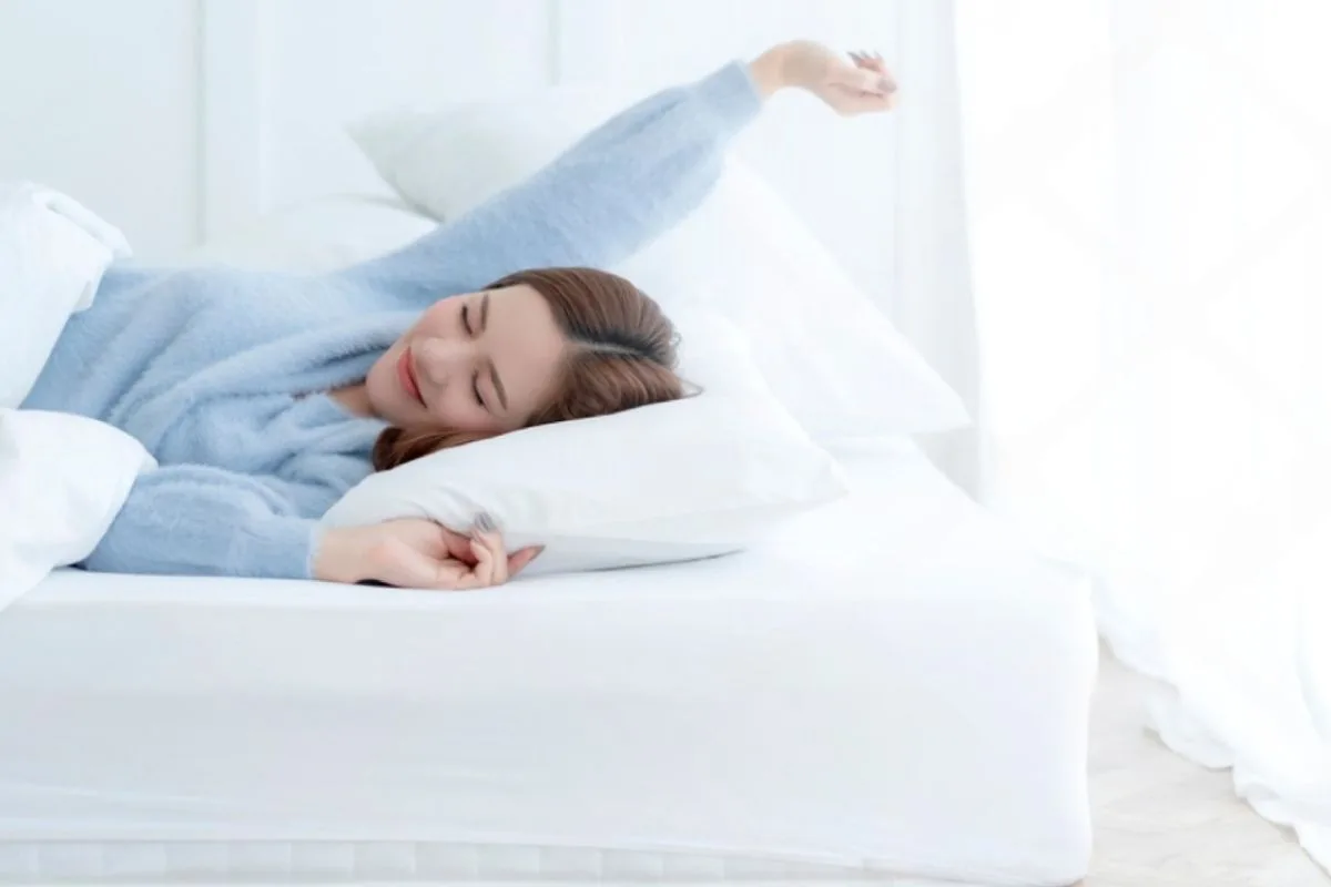 What Is the Difference Between Foam and Latex Mattress? Woman waking up comfortably on a mattress, illustrating how mattress material can affect sleep quality and comfort