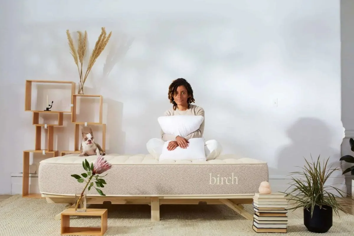 Person sitting on a Birch Natural Mattress with pillows, highlighting proper mattress care to help maintain warranty coverage