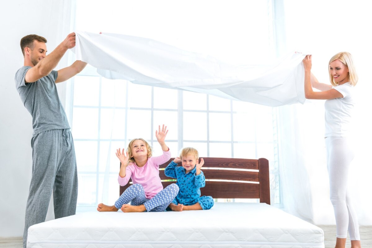 A man and a woman lifting a blanket while a boy and a girl sit on a bed.