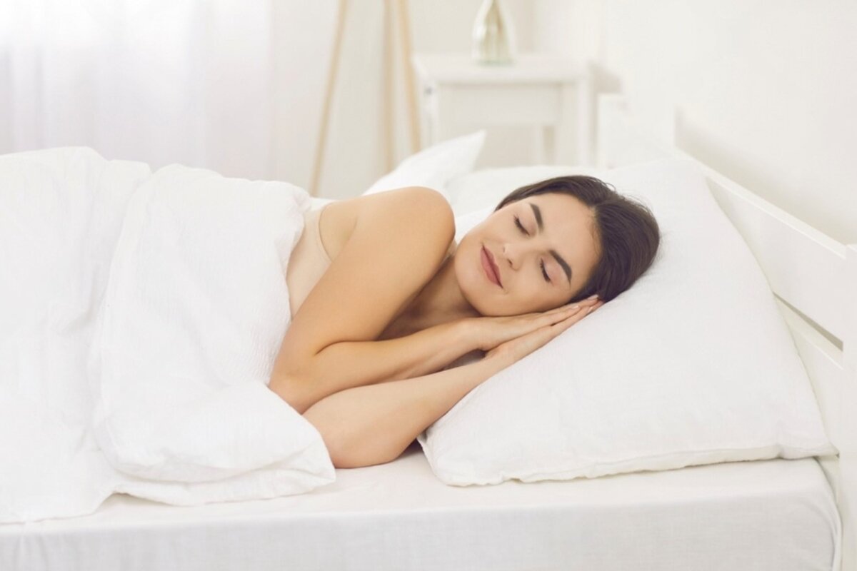 A woman sleeping on a white bed.