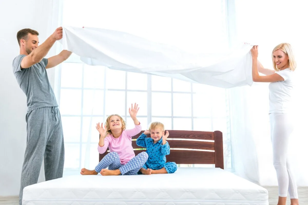 How Important Is an Organic Mattress? A man and a woman holding a blanket while a girl and a boy sit on the bed.