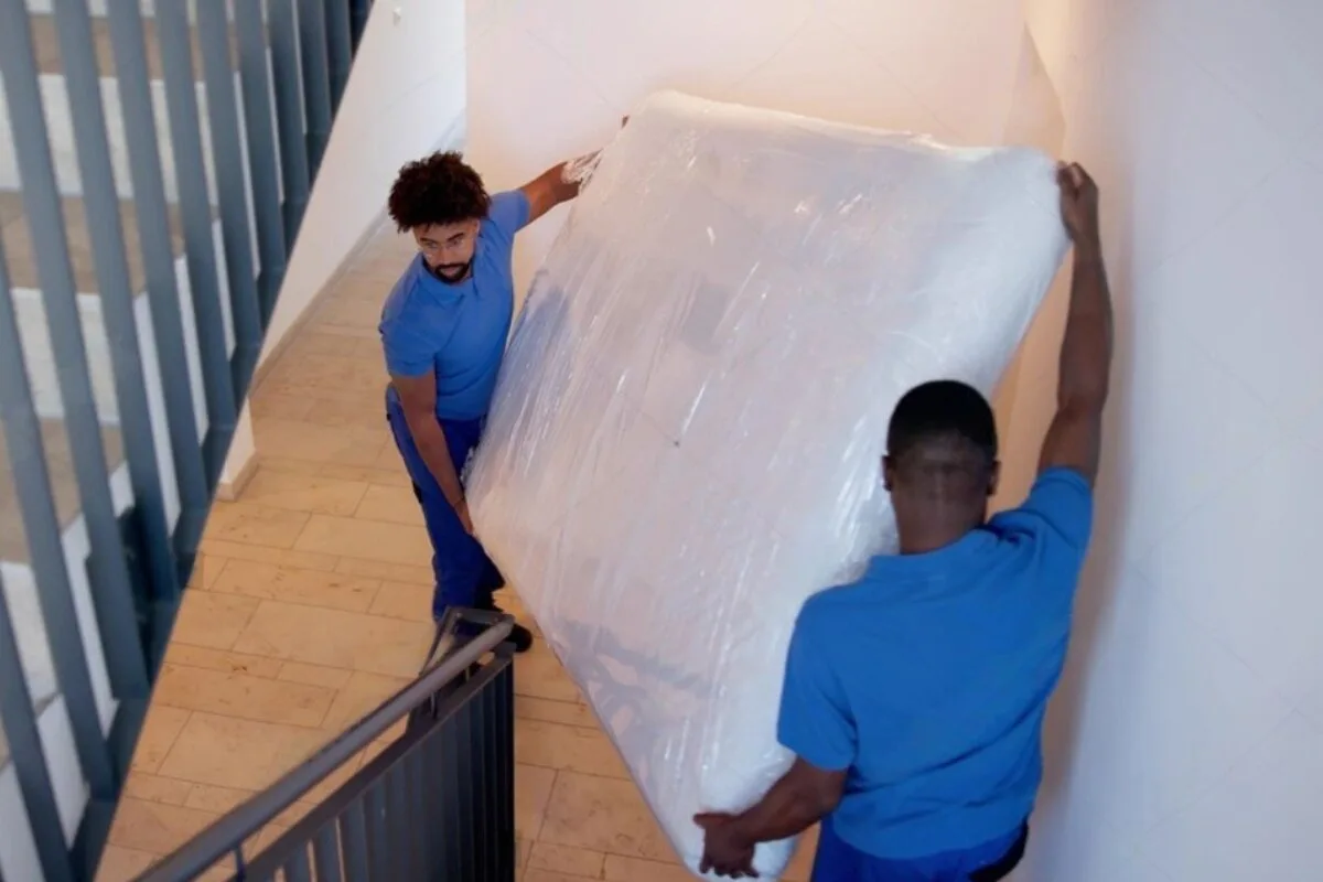 How to Move a Latex Hybrid Mattress? 2 men wearing blue moving a mattress down the stairs.