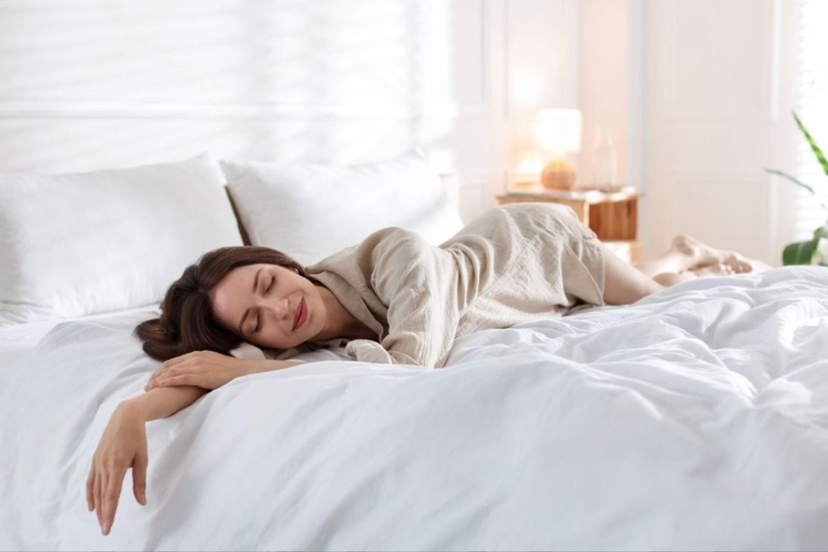 A woman sleeping on a bed with her hand sticking out.