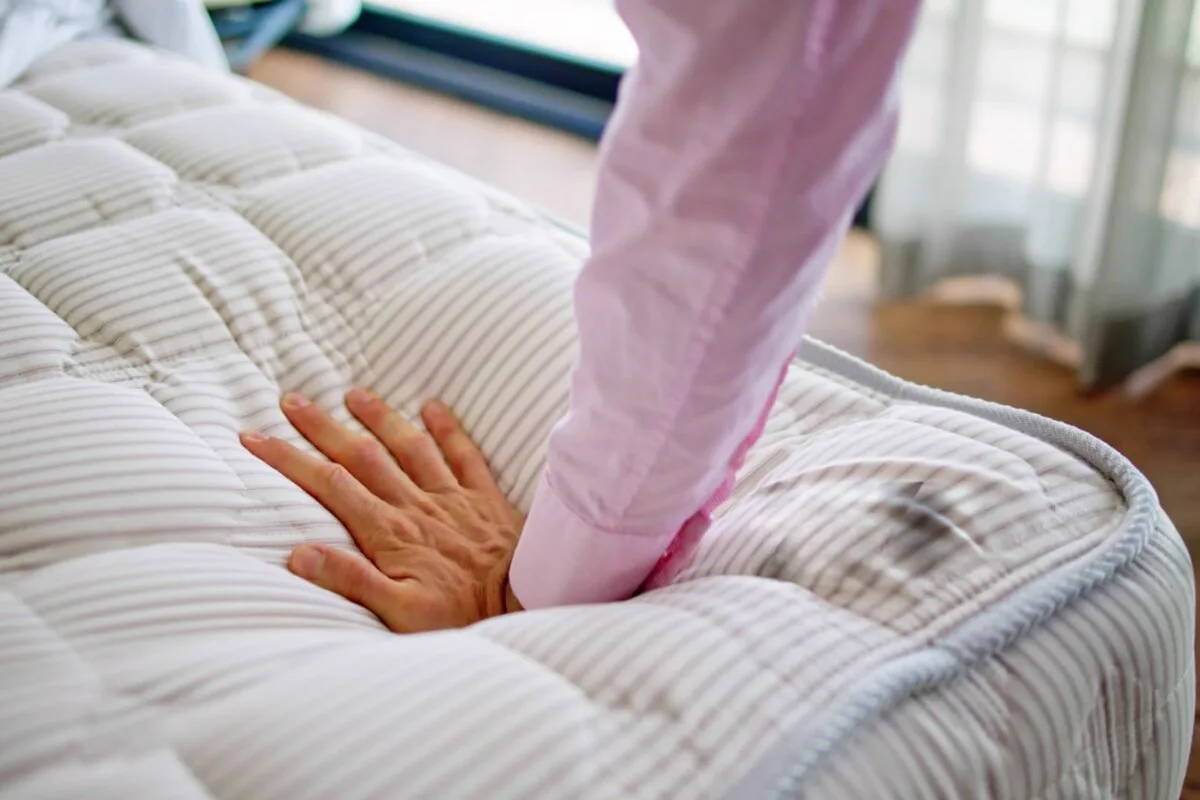 Is It Healthy to Sleep On An Adjustable Firmness Mattress? A person with a pink long sleeve pressing on a bed.