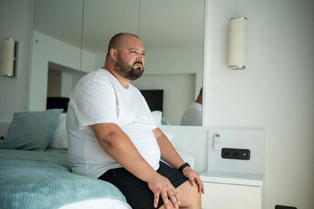 Is a Memory Foam or Hybrid Mattress Better for a Heavy Person? Heavy person sitting on the edge of a mattress to illustrate edge support and durability for higher body weights