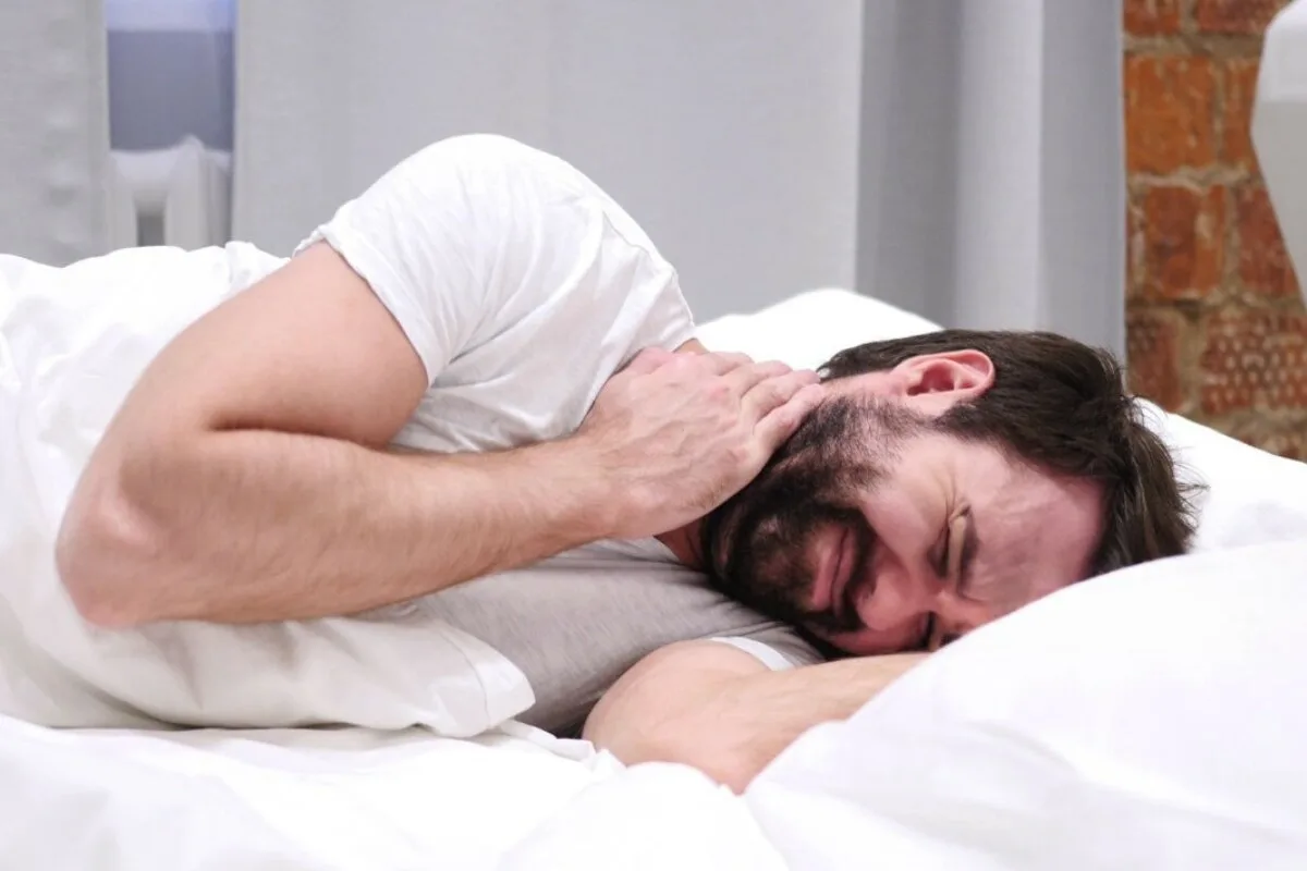Is a Plush Mattress Good for Stomach Sleepers? A man holding his neck in pain while he is on a bed.