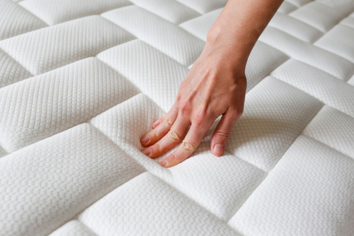 Hand pressing into a mattress surface to demonstrate softness and identify areas where additional support may be needed to create a firmer feel.