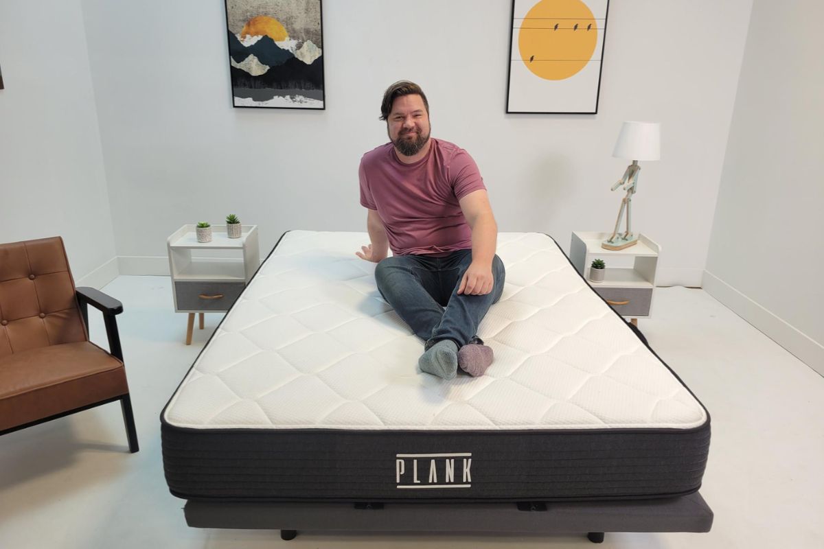 Reviewer sitting on a Plank Firm Luxe mattress during the sleep trial period, demonstrating the at-home testing experience for new owners