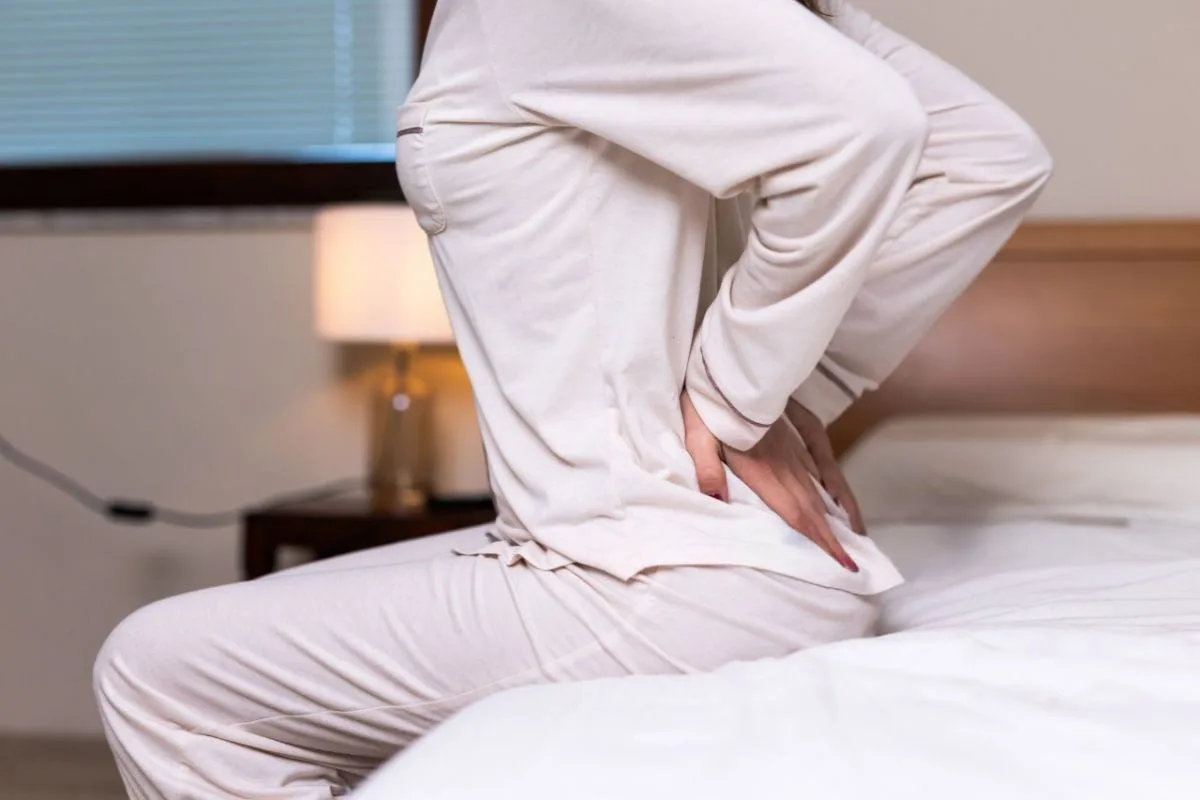 What Firmness Is Best for Combination Sleepers? Person sitting on a mattress with lower back discomfort, highlighting the importance of choosing the right firmness level for proper spinal support