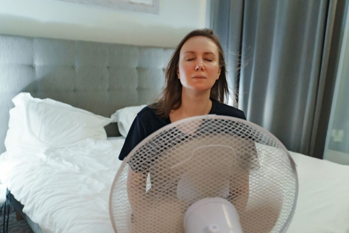 Person using a fan while sleeping to stay cool alongside a cooling mattress during warm nights