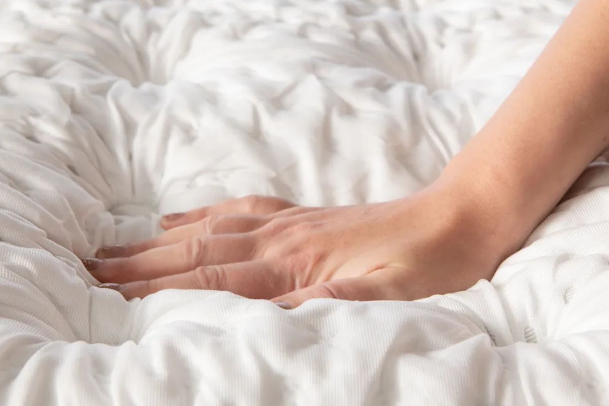 Hand pressing into a plush mattress surface to demonstrate the deep cushioning and soft comfort that define a plush mattress.