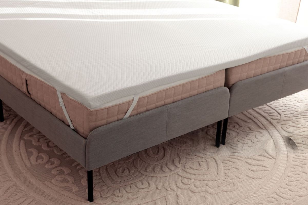 Memory foam mattress topper secured with corner straps, showing a common solution used to add cushioning and improve back pain relief on an existing mattress