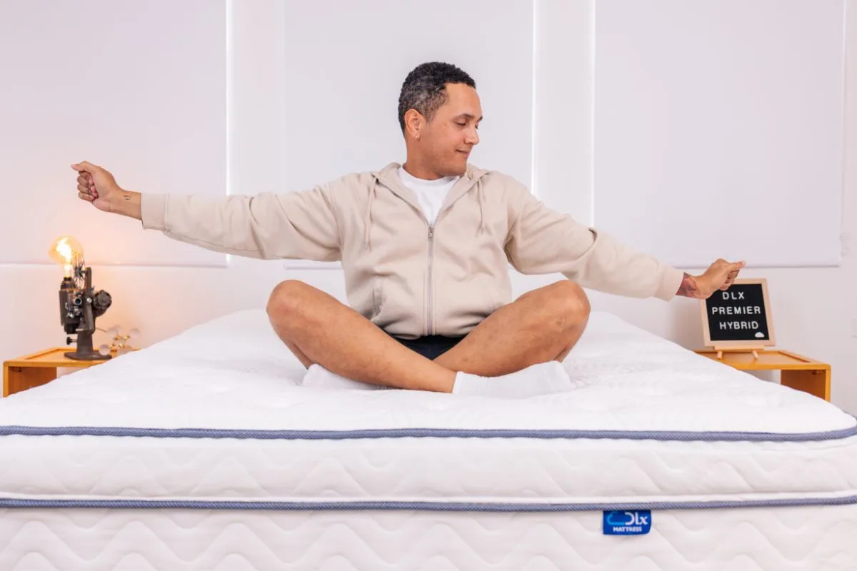 Person sitting on the edge of the DLX Premier Hybrid mattress demonstrating strong edge support and maximum weight capacity