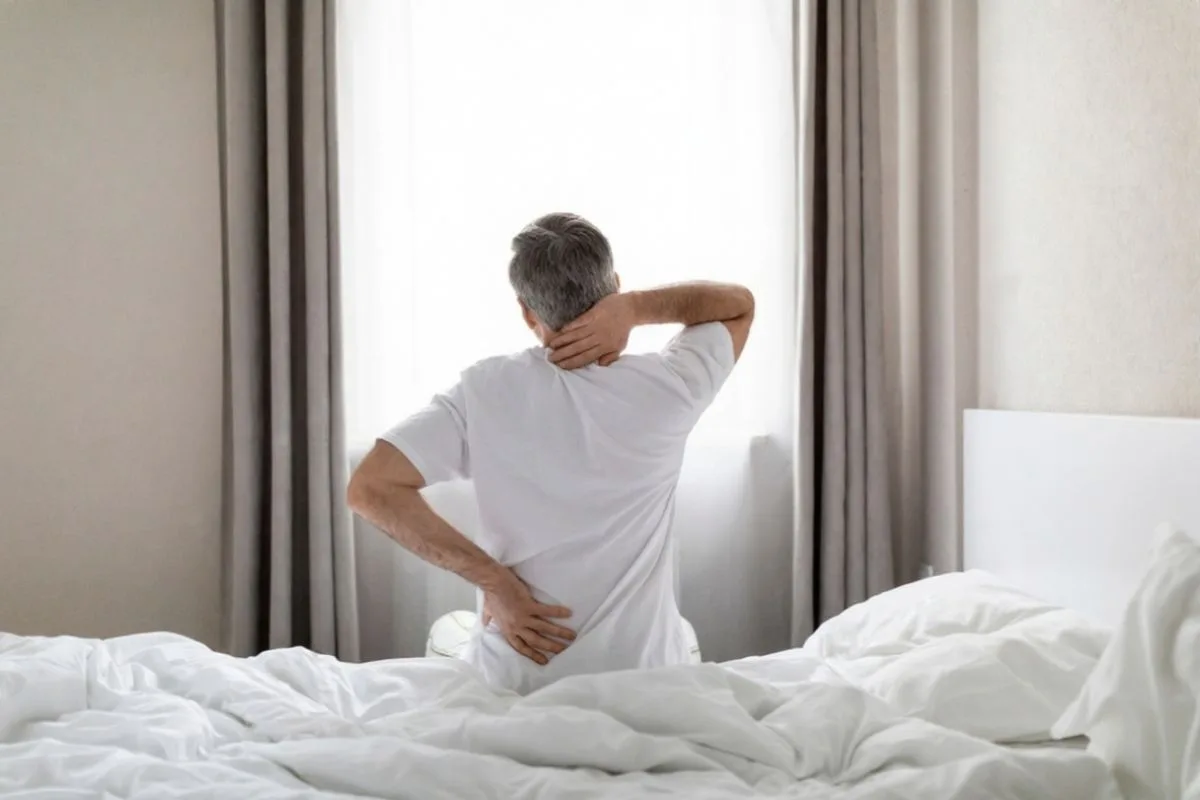 How to Prevent Back Pain for Combination Sleepers? Older adult waking up with back and neck pain, illustrating the impact of poor sleep posture and inadequate mattress support