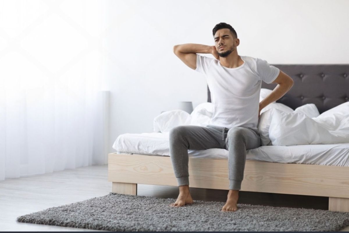 Person experiencing neck and lower back pain after sleeping, highlighting the importance of proper support for combination sleepers
