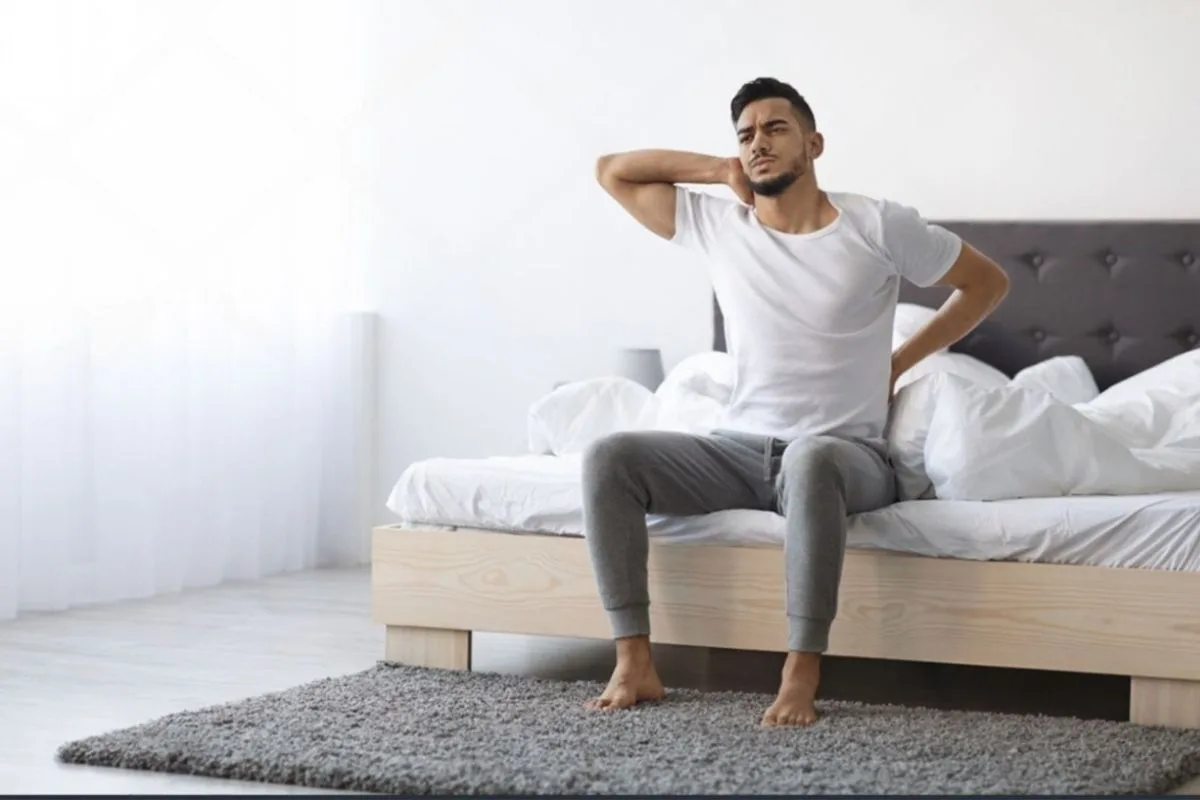 Person experiencing neck and lower back pain after sleeping, highlighting the importance of proper support for combination sleepers