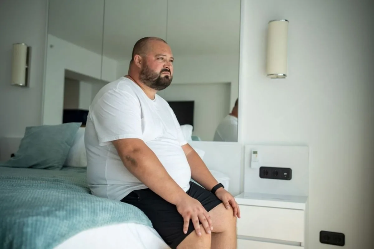 Heavy person sitting on the edge of a mattress, highlighting the importance of strong edge support and stability for easier sitting and getting in and out of bed